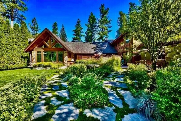 A log cabin with a sloped roof, surrounded by dense greenery and tall trees. - Lakefront Legacy luxury Lake Tahoe Estate Camp Richardson luxe01 (South Lake Tahoe)