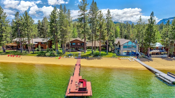 A resort with multiple wooden cabins, a dock extending into a clear lake, and a sandy beach. - Lakefront Legacy luxury Lake Tahoe Estate Camp Richardson luxe01 (South Lake Tahoe)