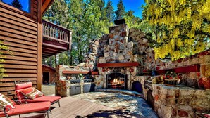A stone fireplace with a fire, surrounded by a wooden deck and red lounge chairs. - Lakefront Legacy luxury Lake Tahoe Estate Camp Richardson luxe01 (South Lake Tahoe)