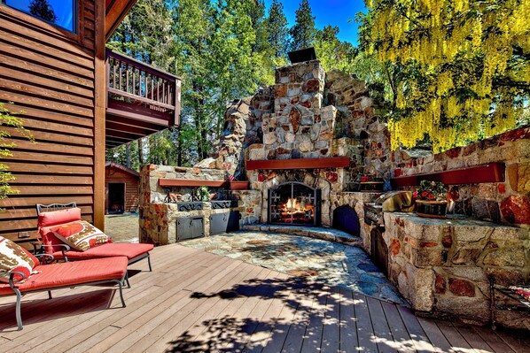 A stone fireplace with a fire, surrounded by a wooden deck and red lounge chairs. - Lakefront Legacy luxury Lake Tahoe Estate Camp Richardson luxe01 (South Lake Tahoe)