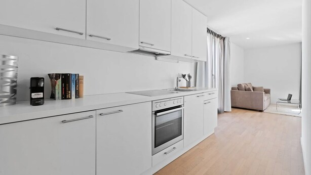 Una cocina moderna con armarios blancos, horno empotrado y encimera con libros y hervidor.