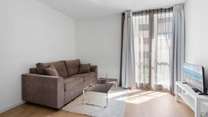 Una sala de estar moderna con un sofá marrón, una mesa de centro de vidrio y un televisor sobre un mueble blanco.