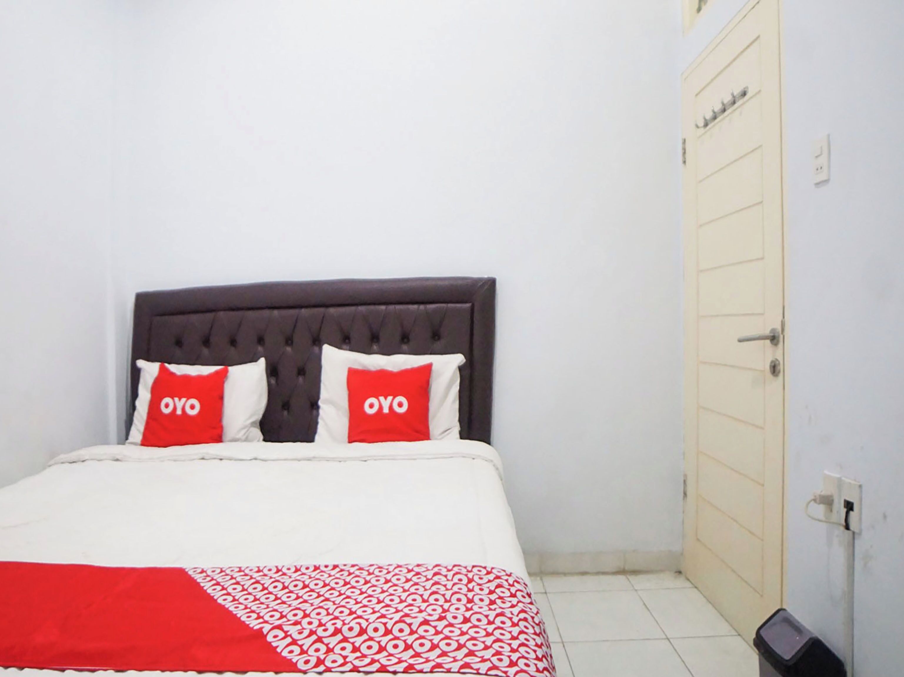 A bed with a dark headboard, two pillows with 'OYO' text, and a patterned red and white blanket.