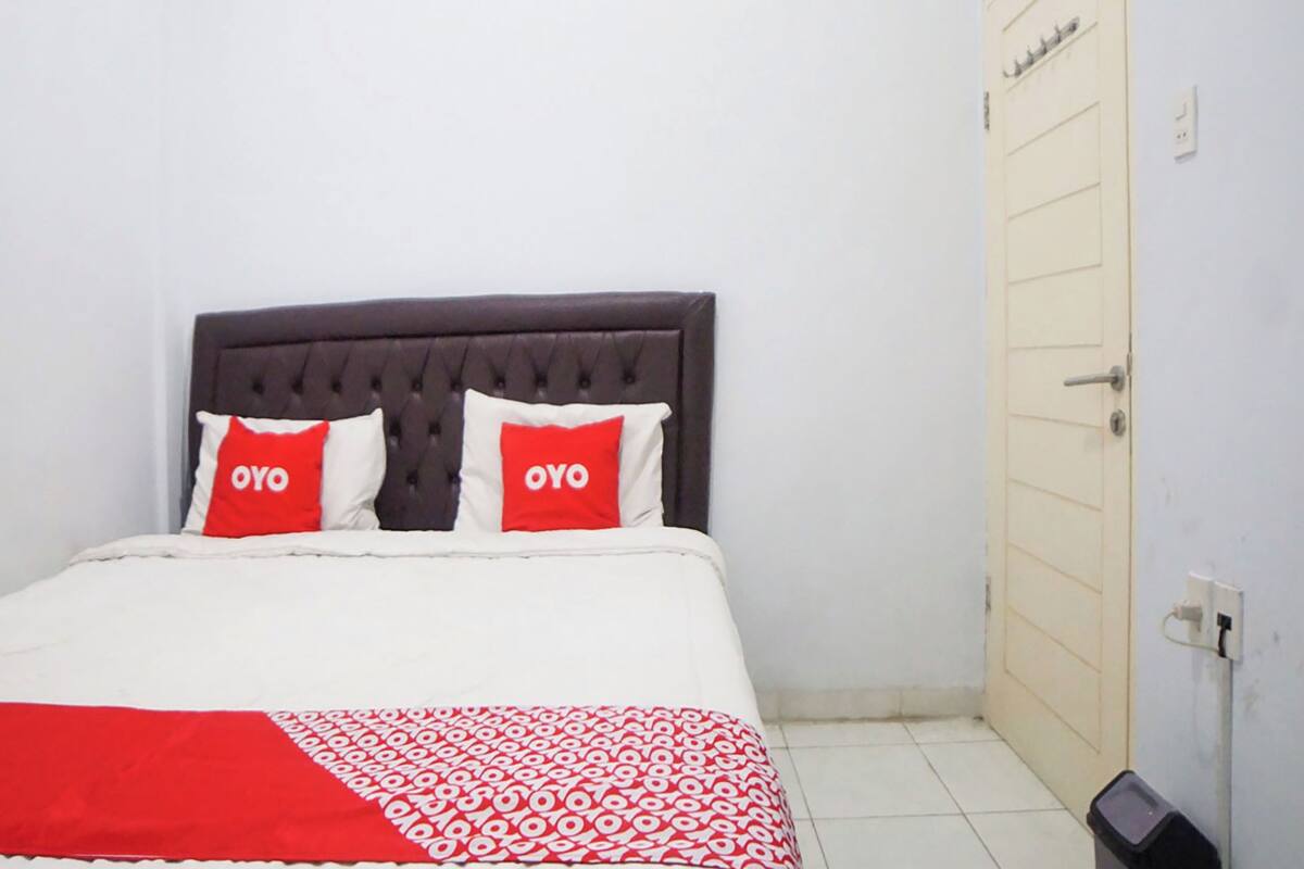 A bed with a dark headboard, two pillows with 'OYO' text, and a patterned red and white blanket.