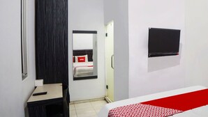 Une chambre d’hôtel de taille réduite, comprenant un lit, un petit bureau, une chaise, un miroir et un téléviseur fixé au mur.