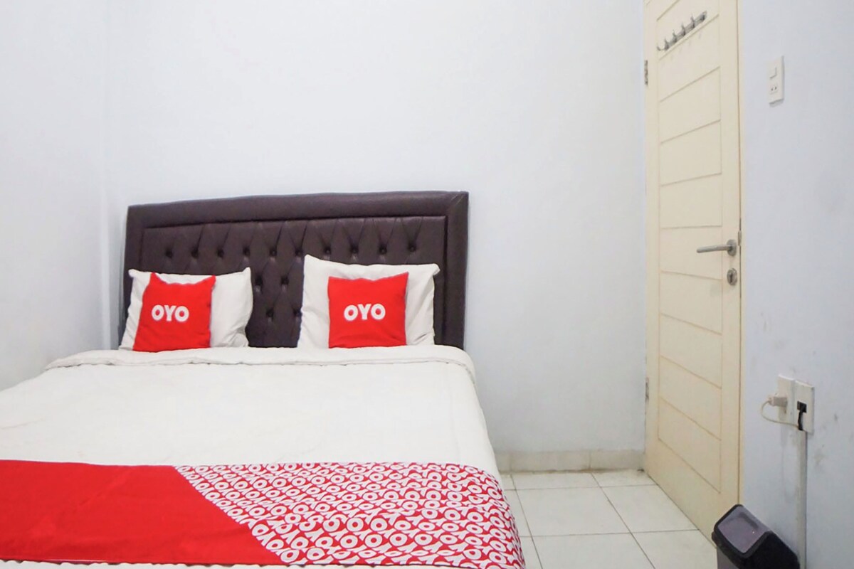 Ein Bett mit dunklem Kopfteil, zwei Kissen mit dem Schriftzug 'OYO' und einer rot-weißen, gemusterten Decke.