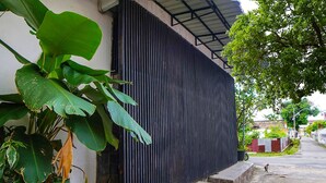 Un bâtiment à l’extérieur en métal ondulé, avec un chemin en béton et une grande plante verte au premier plan.