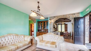 A spacious living room with a sofa, a patterned rug, and a stone archway leading to a kitchen. - Beautiful Apt With Seaview Terrace (Pisciotta)