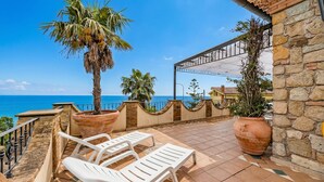 A terrace with white lounge chairs, a palm tree, and a view of the sea. - Beautiful Apt With Seaview Terrace (Pisciotta)