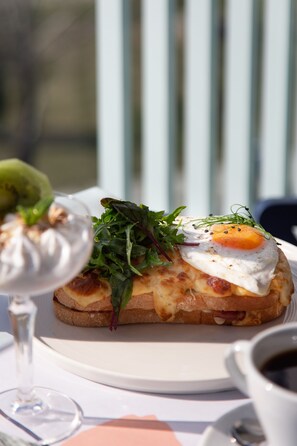 A sandwich with a fried egg on a slice of bread, accompanied by a glass of white wine and a cup of coffee on a table.