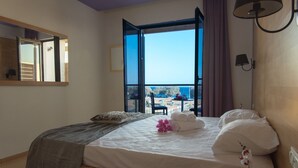Un dormitorio con una cama grande, vista al mar y un balcón con mesa y sillas.