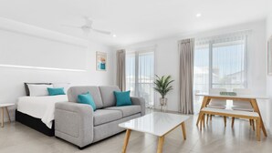 A modern living room with a grey sofa, a white coffee table, and a dining table with chairs. - Coastal Breeze 12a - Kingscliff Studio (Kingscliff)