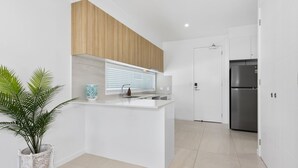 A modern kitchen with white cabinetry, a built-in island, and a stainless steel refrigerator. - Coastal Breeze 12a - Kingscliff Studio (Kingscliff)