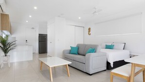 A modern, well-lit living room with a grey sofa, teal cushions, a white coffee table, and a bed with white bedding. - Coastal Breeze 12a - Kingscliff Studio (Kingscliff)