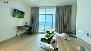Quarto moderno com uma janela grande, uma escrivaninha, duas cadeiras verdes e uma mesa de jantar com xícara e pires.