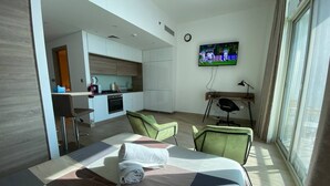 Quarto de hotel com uma cama, televisão fixada na parede, escrivaninha e uma cadeira.