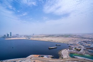 An aerial view of a coastal area with a large body of water, industrial buildings, and a sandy beach.