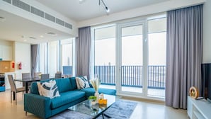 Una sala moderna con un sofá color turquesa, una mesa de centro de vidrio y un amplio ventanal corredizo que da a un balcón.