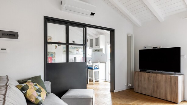 Un salon moderne avec un canapé, un téléviseur posé sur un meuble en bois et une grande fenêtre.