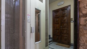 Un pasillo con una puerta metálica, una puerta de madera con diseños circulares y un suelo de mármol.