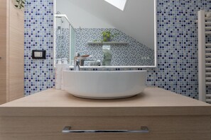Une salle de bain avec un lavabo rond blanc, un miroir et une douche.
