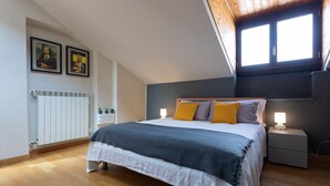 Un dormitorio con cama, mesitas de noche, un radiador y dos ventanas.
