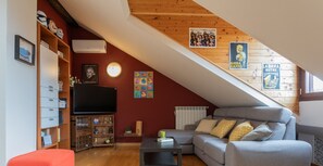 A cozy loft apartment with a sloped ceiling, a grey sofa, a small table, and a bookshelf.