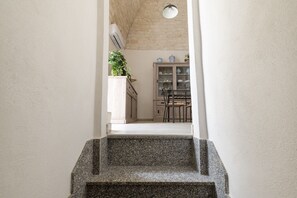 Staircase leads to a dining area with a wooden cabinet and potted plant.