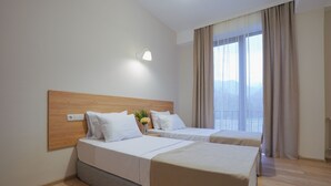 Ein Hotelzimmer mit zwei Betten, einem hölzernen Kopfteil, einem Nachttisch mit Lampe und einem großen Fenster mit Vorhängen.
