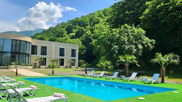 Ein modernes Hotel mit Schwimmbad, Liegestühlen und einer üppigen Grünanlage.