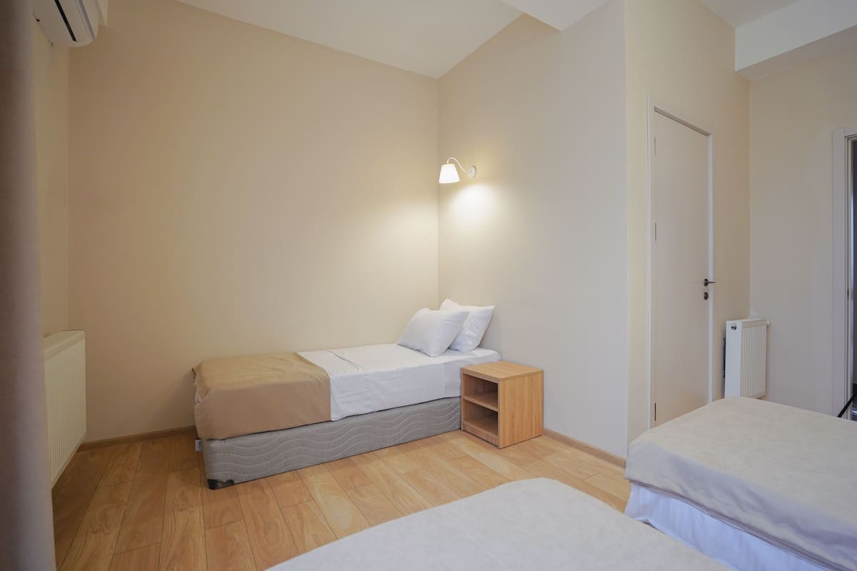 A small, clean room with a single bed, a nightstand, and a wall-mounted light.