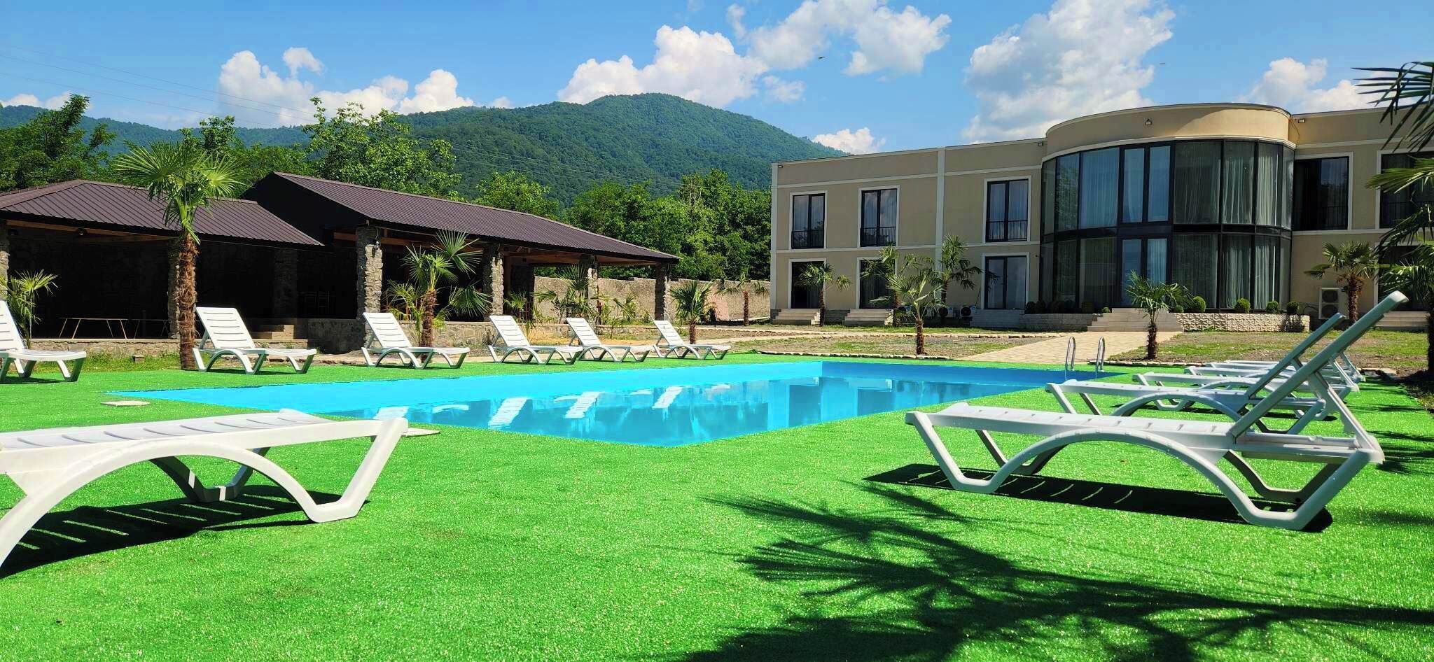 A swimming pool with artificial grass, lounge chairs, and a mountain backdrop.