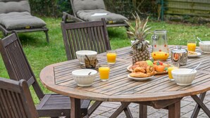 Een ronde houten tafel buiten gedekt met ontbijtartikelen, zoals een ananas, sinaasappelsap en gebak.