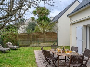 Een terras met een ronde houten tafel en stoelen, omringd door een houten hek en een gazon.