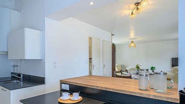 Een moderne keuken met een centraal eiland, inbouwapparatuur en een zichtbare eethoek op de achtergrond.