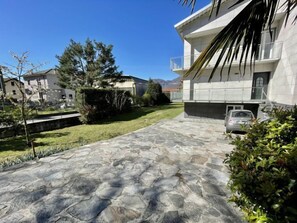 Un bâtiment moderne avec une allée pavée de pierres, une voiture garée dans le garage et un ciel bleu dégagé.