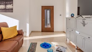 Een woonkamer met een bruine leren bank, een houten deur, een witte kast en een flatscreen televisie op een standaard.