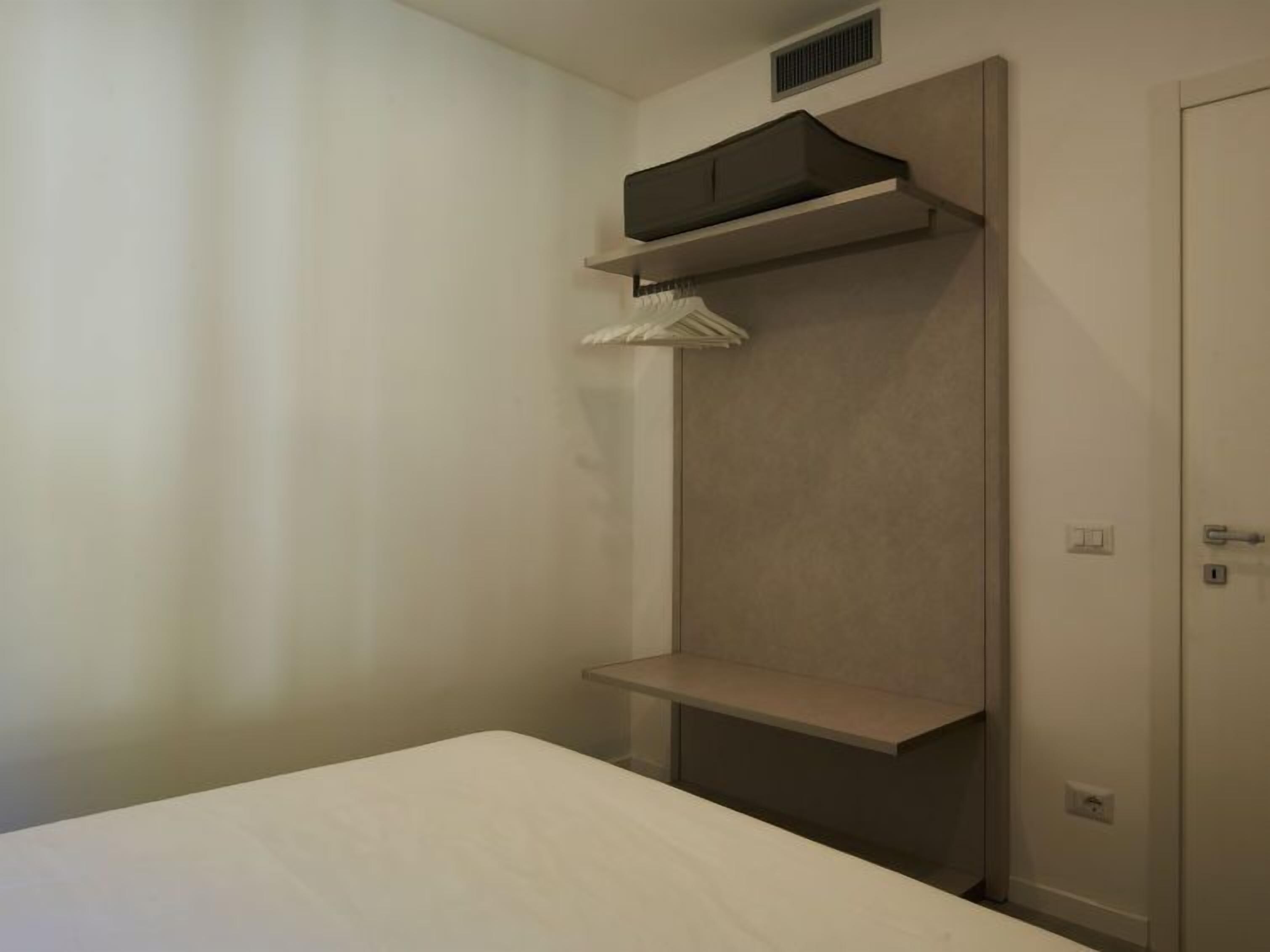 Une pièce au décor minimaliste, avec un lit, une armoire et une étagère.