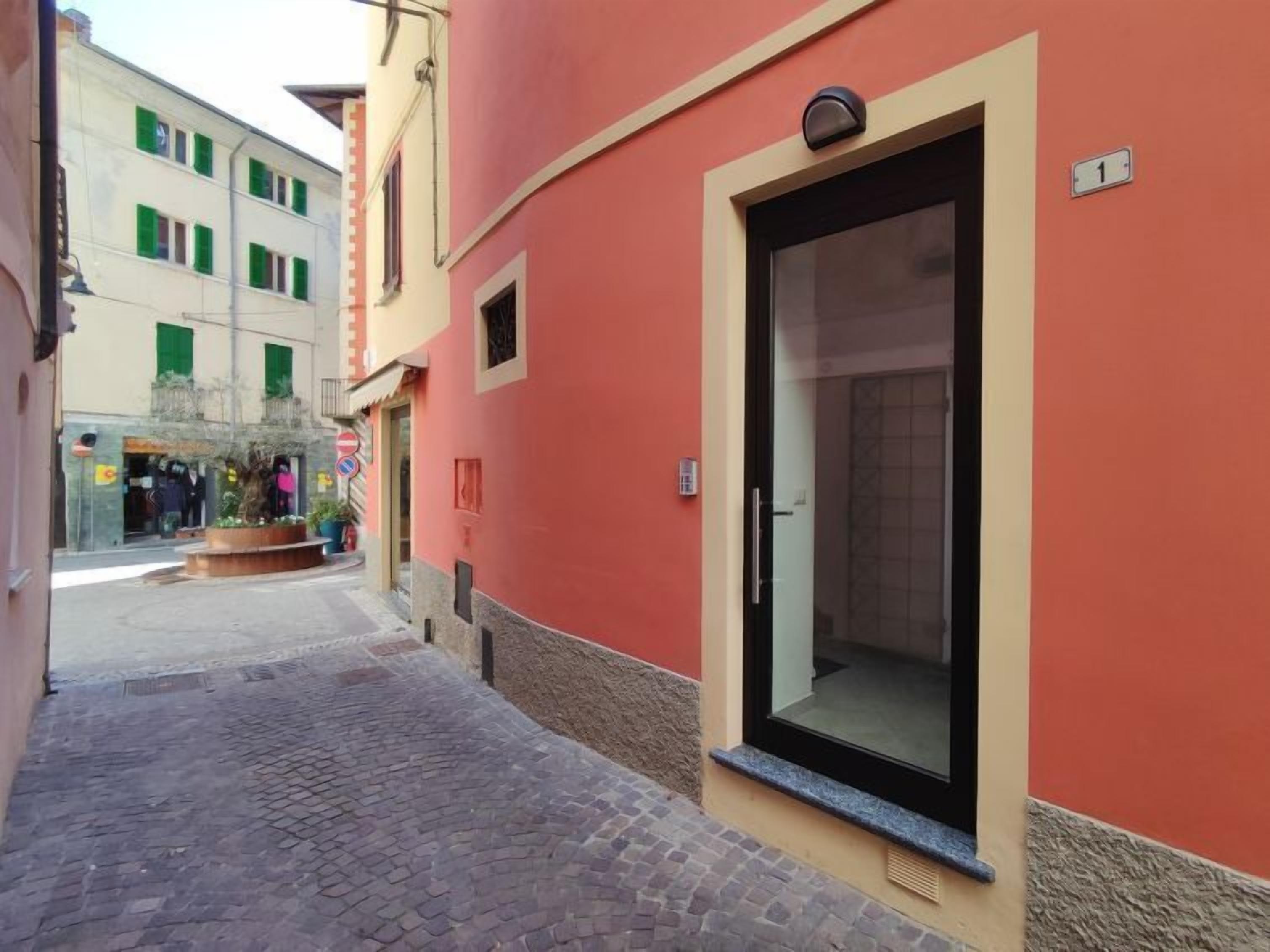 A narrow cobblestone street with a red building featuring a large glass door and a small window.