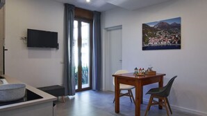 Une cuisine moderne avec un évier en pierre, un coin repas avec une table et des chaises en bois, un téléviseur fixé au mur et un tableau représentant une ville côtière.
