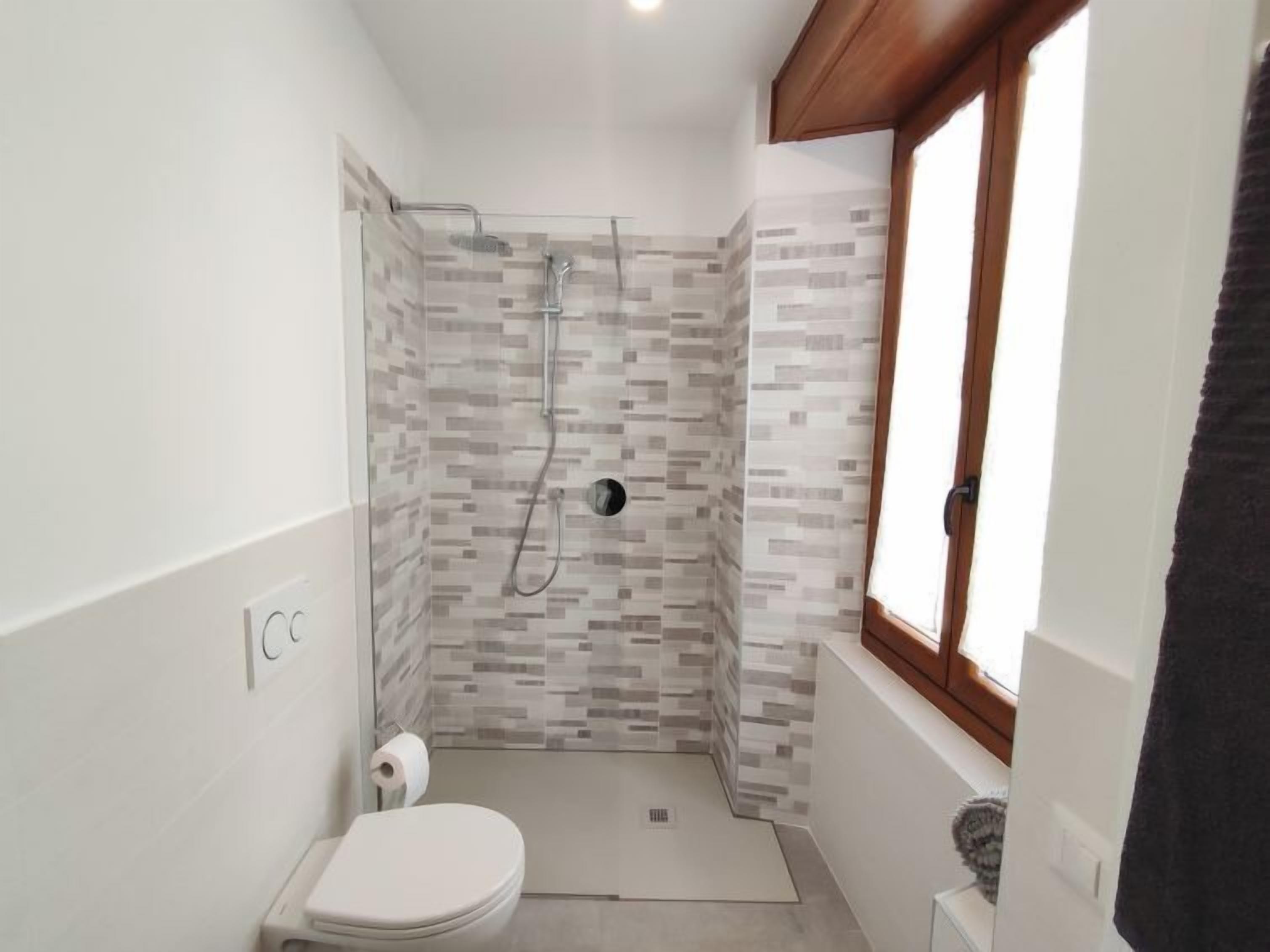 A small, modern bathroom with a shower, toilet, and a window.