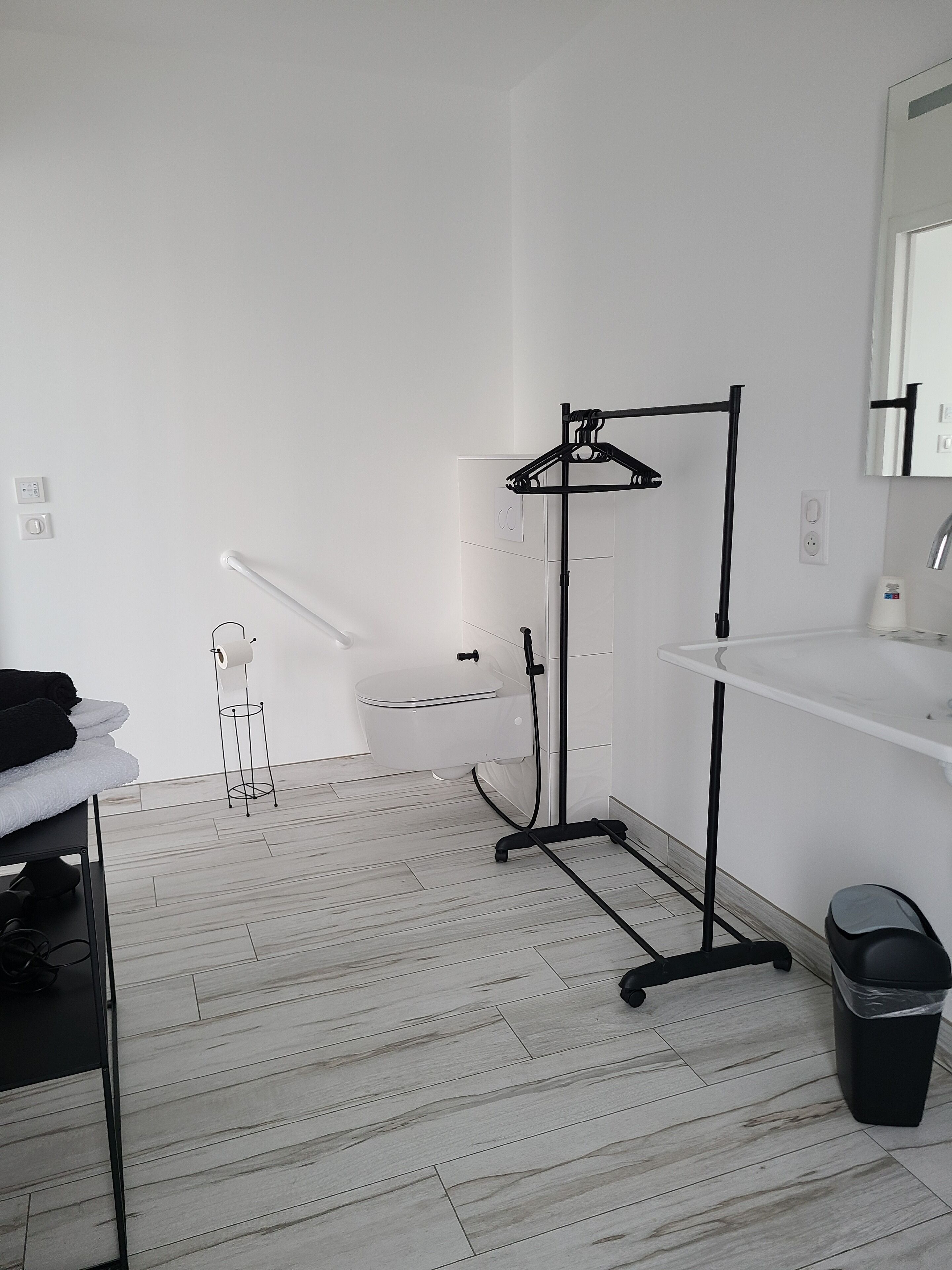 A modern bathroom with a white sink, a mirror, a toilet, and a black towel rack.