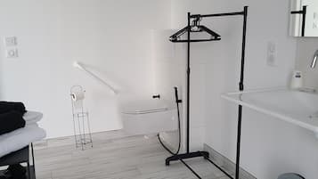 A modern bathroom with a white sink, a mirror, a toilet, and a black towel rack.