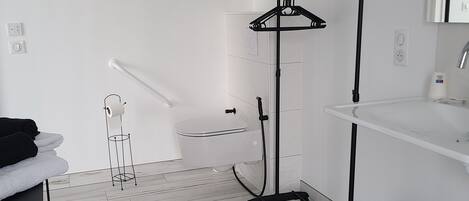 A modern bathroom with a white sink, a mirror, a toilet, and a black towel rack.