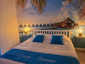 A bedroom with a bed, pillows, and a view of overwater bungalows. - L'escale Romanesque (Ozeville)