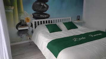 A bedroom with a white bed, green pillows, a green throw blanket, and a wall mural of stacked stones.