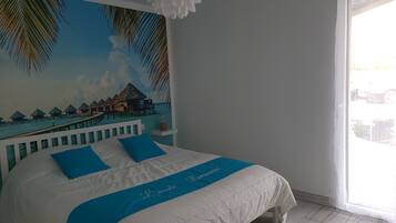 Un dormitorio con cama, un mural de una playa y un ventilador de techo blanco.