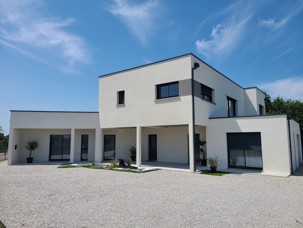 A modern two-story house with a gravel driveway and potted plants. - L'escale Romanesque (Ozeville)