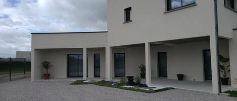 A modern two-story building with a covered patio area, large windows, and a gravel driveway.