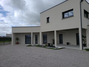 A modern two-story building with a covered patio area, large windows, and a gravel driveway. - L'escale Romanesque (Ozeville)